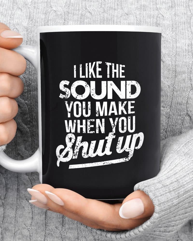 Hands hold a black coffee mug with white text that says I like the sound you make when you shut up.