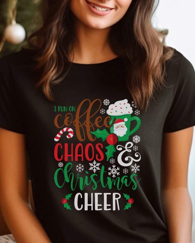 Woman wearing a black T-shirt with a Christmas design featuring coffee, Santa, and the text: I run on coffee, chaos, and Christmas cheer.