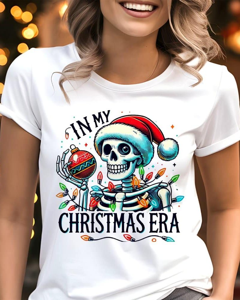 White t-shirt featuring a skeleton wearing a Santa hat, holding an ornament, surrounded by Christmas lights; text reads In My Christmas Era.