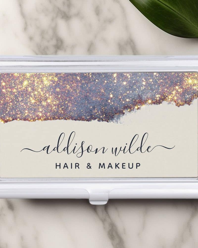 Silver business card holder with a design featuring a gold and purple glitter watercolor wash and the name Addison Wilde, Hair & Makeup.