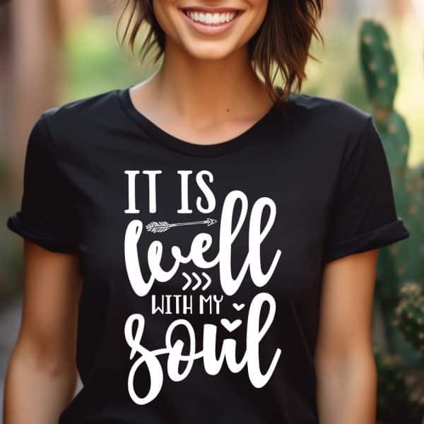Woman Wearing A Black T-Shirt With The Phrase It Is Well With My Soul In White Lettering. An Arrow Is Included In The Design.