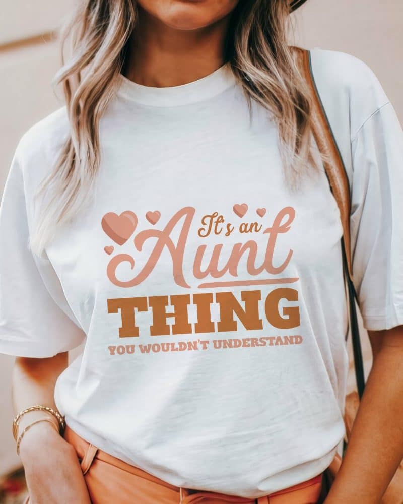 Woman wearing a white t-shirt with the text Its an Aunt Thing in a peachy-brown font.