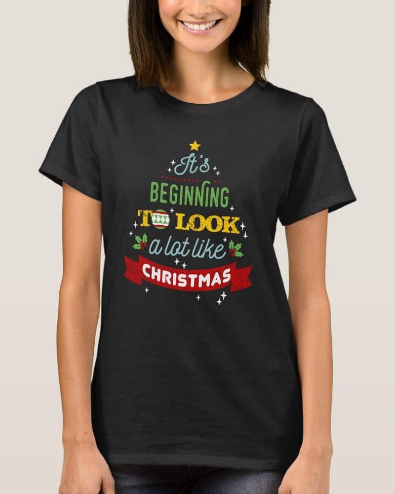 Woman wearing a black t-shirt with a Christmas tree design that says, Its beginning to look a lot like Christmas.