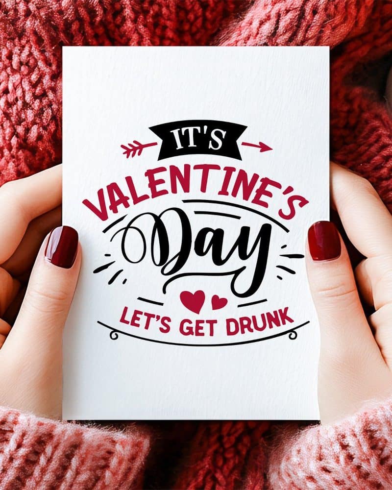 Two hands hold a Valentines Day card that says, Its Valentines Day, Lets Get Drunk.
