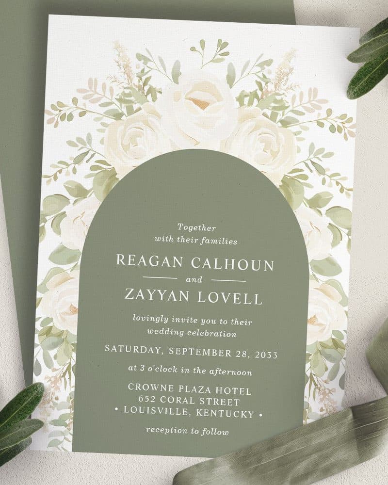 Wedding invitation with white roses and greenery, featuring the names Reagan Calhoun and Zayyan Lovell.