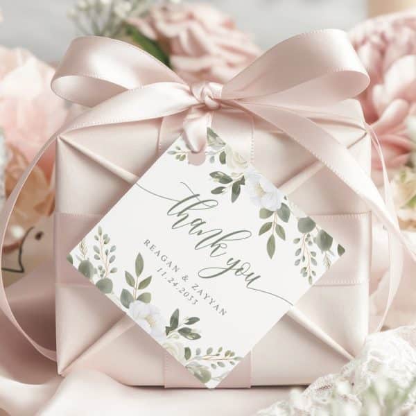 A Wedding Thank You Gift Tag With White Flowers And Green Leaves. The Tag Says Thank You, The Couple'S Names, And Their Wedding Date.