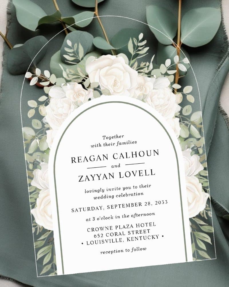 Wedding invitation with arched design, featuring white roses and greenery, announcing the marriage of Reagan Calhoun and Zayyan Lovell.