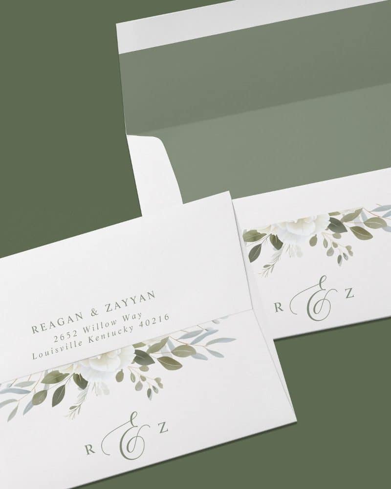 Wedding invitation with white flowers and greenery, featuring the names Reagan & Zayyan and their address.