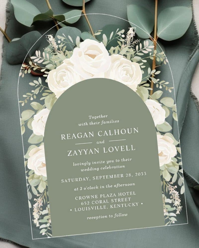 Wedding invitation with white roses and greenery, featuring the names Reagan Calhoun and Zayyan Lovell.