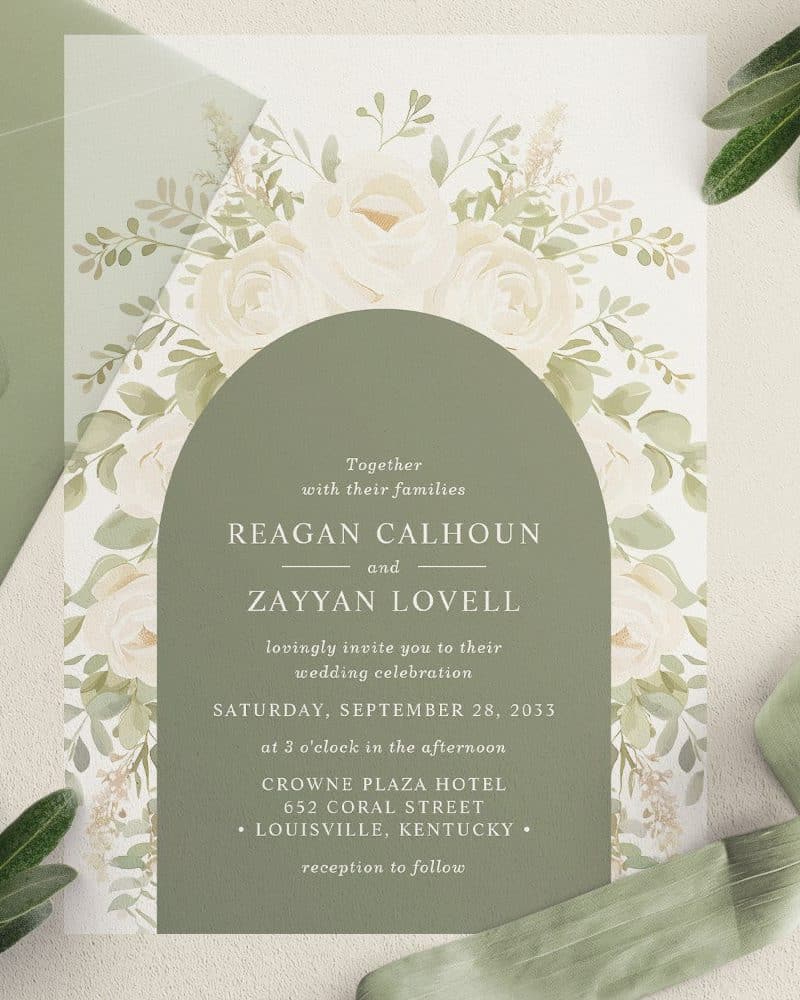 Wedding invitation with white roses and greenery, featuring the names Reagan Calhoun and Zayyan Lovell, and wedding details.