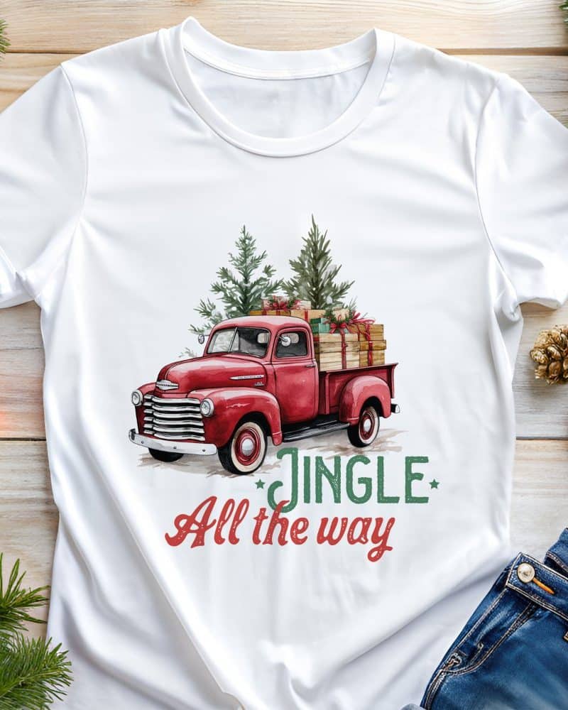 White t-shirt with a red vintage truck carrying Christmas trees and presents. Text reads Jingle All the Way.