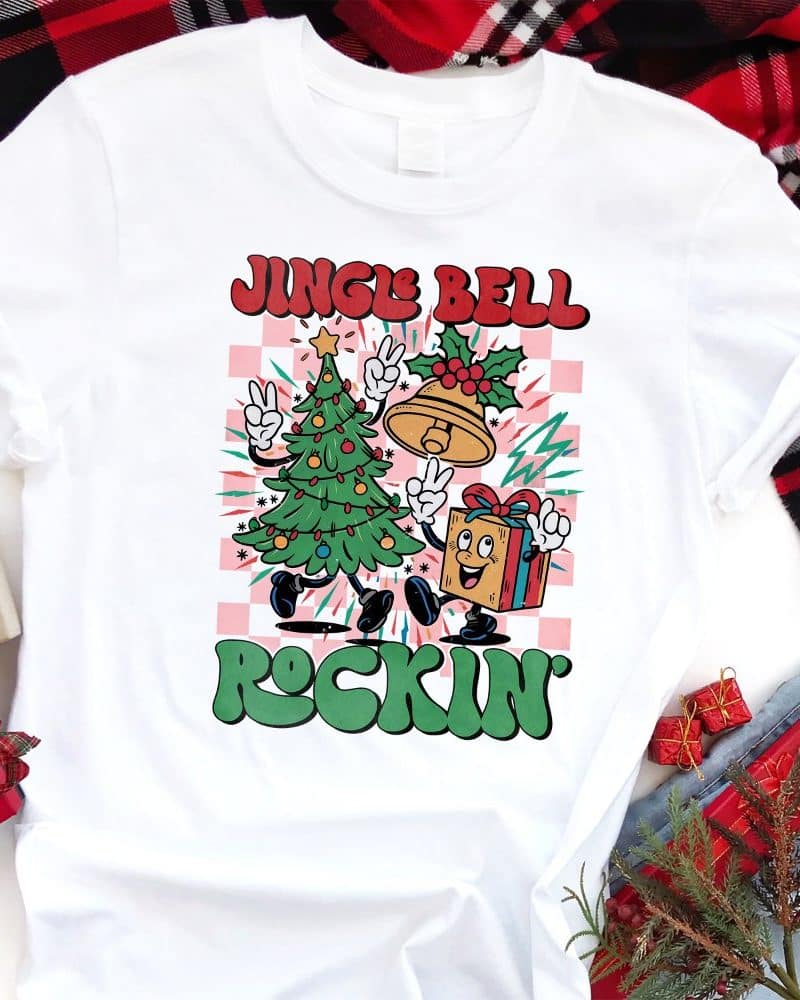 White t-shirt with a Christmas design featuring a cartoon Christmas tree and present dancing. The text Jingle Bell Rockin is included.