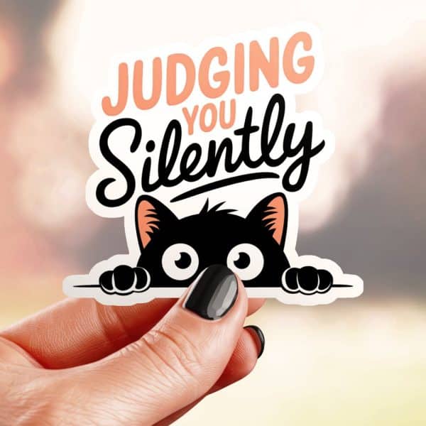 A Hand Holds A Sticker Of A Black Cat Peeking Over A Surface With Text That Says Judging You Silently.