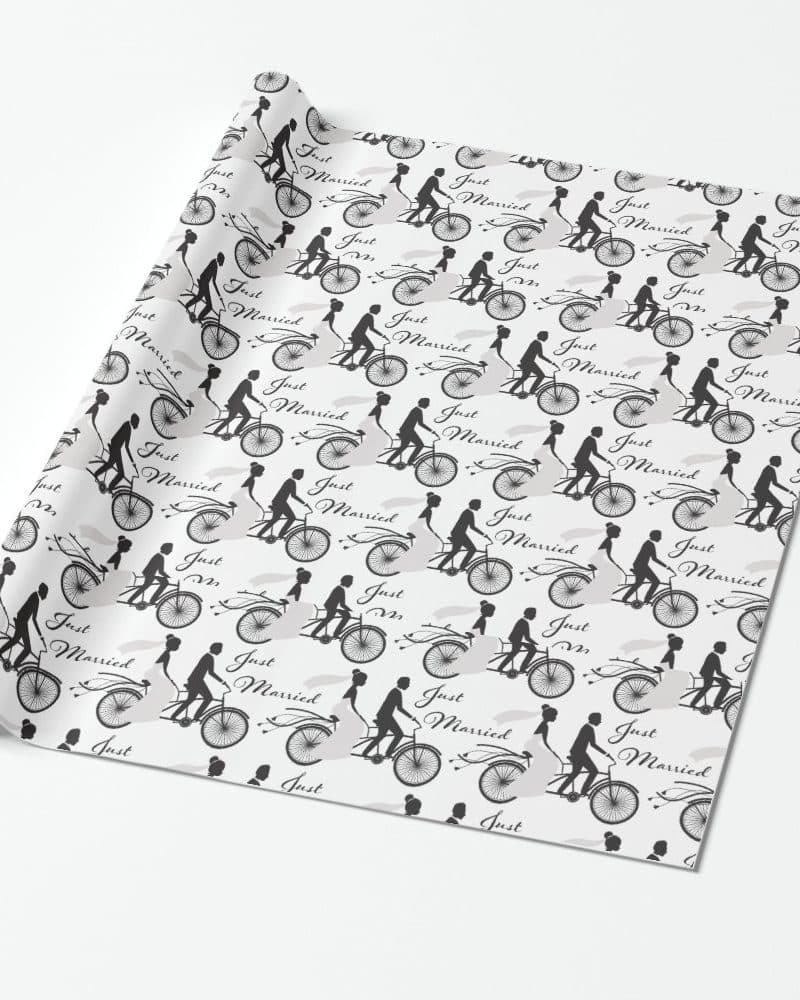 White wedding gift wrap with a repeating pattern of black silhouettes of couples on bicycles; the words Just Married are printed on the wrap.