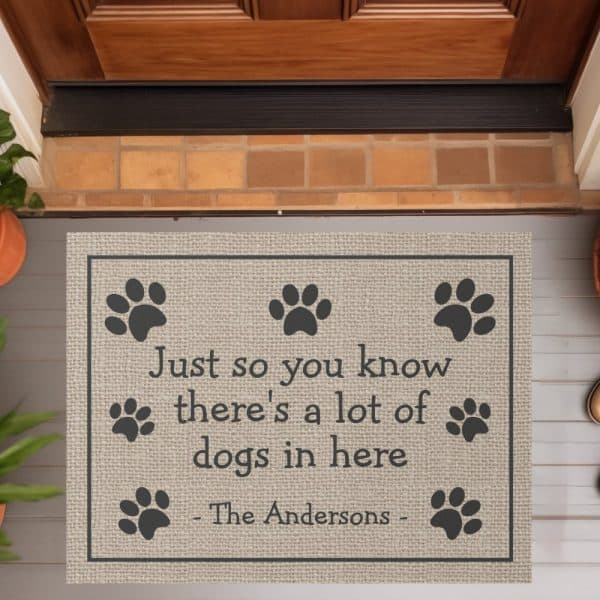 Beige Doormat With Black Paw Prints And Text Reading, &Quot;Just So You Know There'S A Lot Of Dogs In Here - The Andersons -&Quot;.