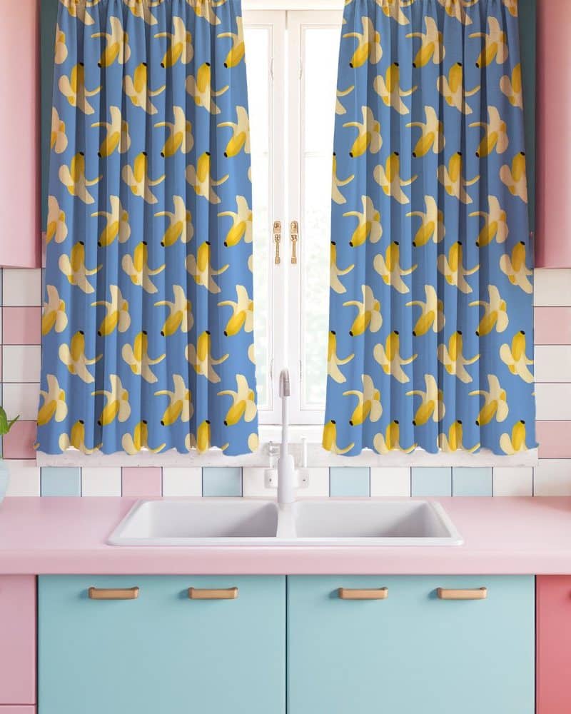 A pair of light blue kitchen curtains with a repeating pattern of yellow bananas.