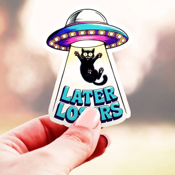 A Hand Holds A Sticker Of A Black Cat Being Abducted By A Ufo. The Sticker Also Says Later Losers.