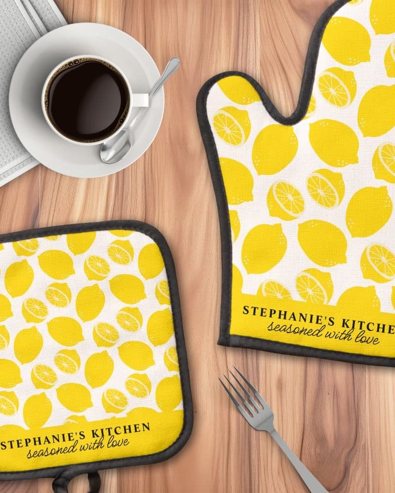 A lemon-printed oven mitt and pot holder set, personalized with the text "Stephanie's Kitchen, seasoned with love".