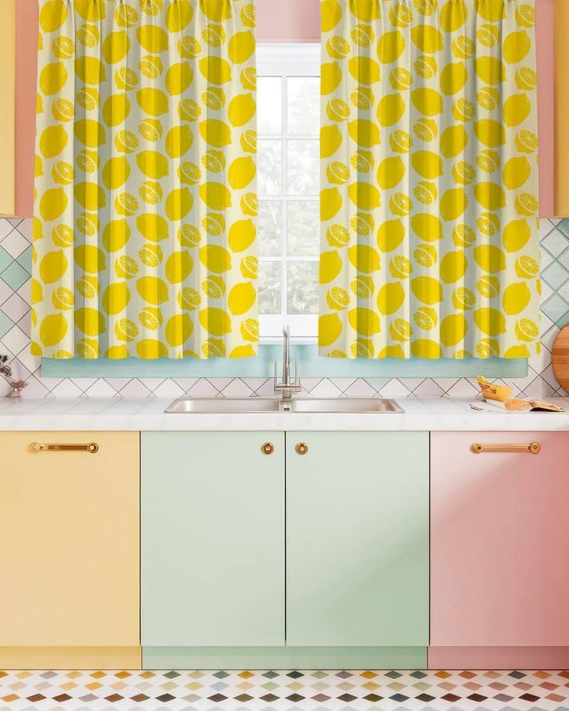 Lemon-printed kitchen curtains hanging above a pastel-colored kitchen sink and cabinets.