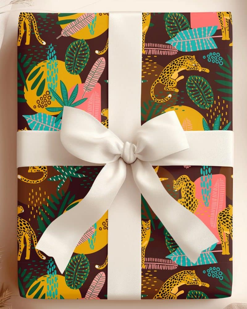A gift wrapped in brown paper featuring a pattern of leopards and tropical leaves, tied with a white ribbon.