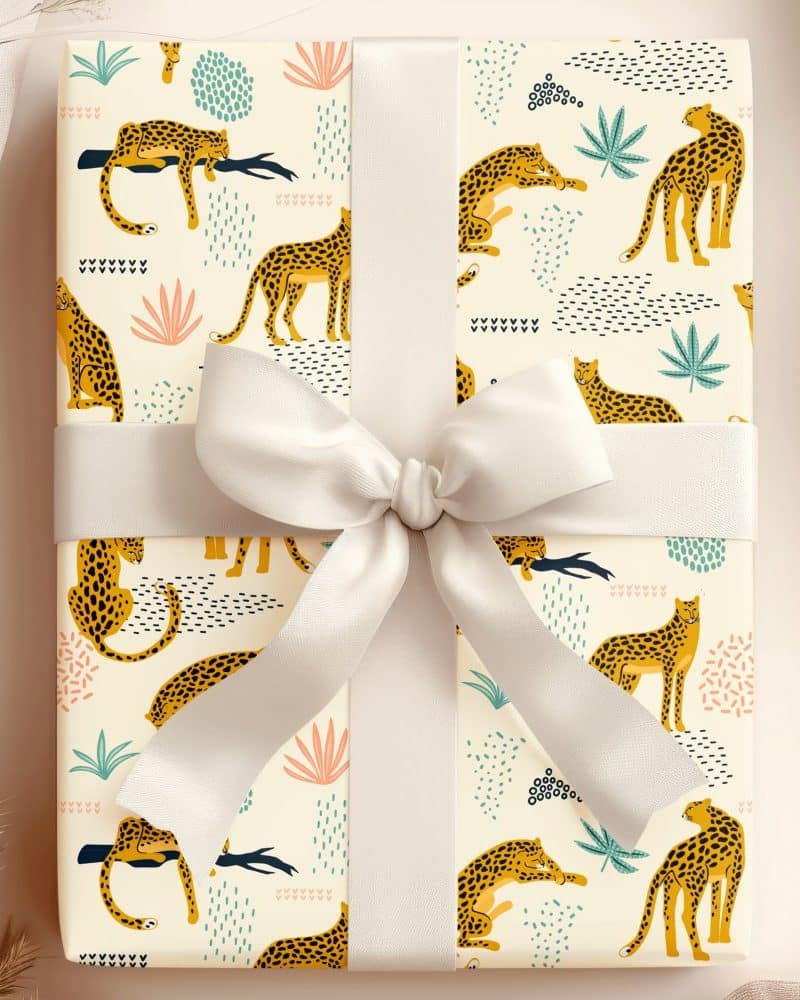 Gift wrapped in off-white paper with a pattern of yellow leopards and abstract shapes. A large off-white bow is tied on top.
