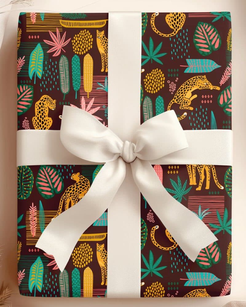 Gift wrapped in dark brown paper featuring a repeating pattern of stylized leopards and tropical leaves. A large off-white bow tops the gift.