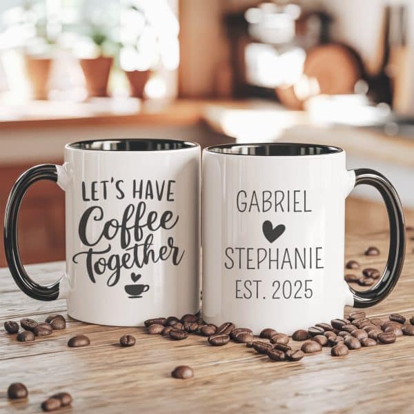 Two White Coffee Mugs With Black Handles And Rims. One Mug Says Lets Have Coffee Together, The Other Says Gabriel Stephanie Est. 2025. Coffee Beans Are Scattered On The Table.
