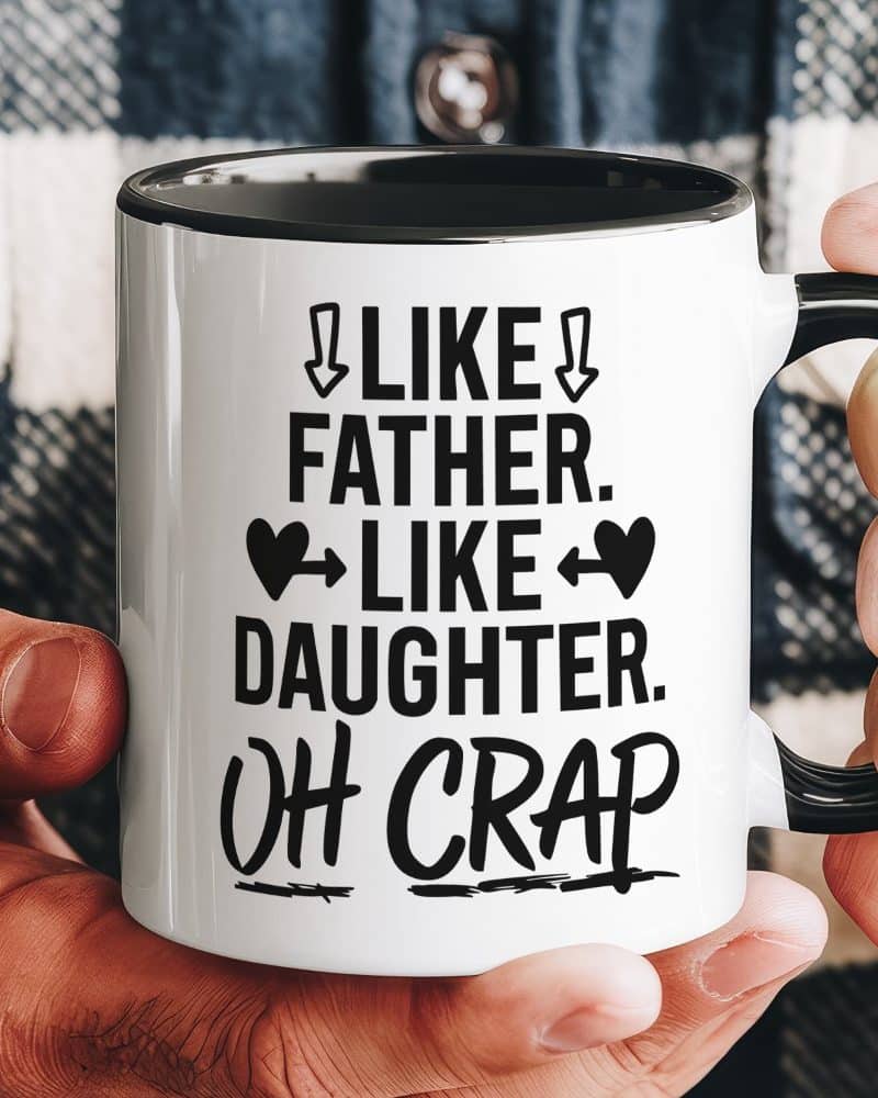 A hand holds a white coffee mug with black text that says Like Father, Like Daughter, Oh Crap.