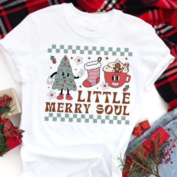 White T-Shirt With A Retro Christmas Design Featuring A Cartoon Christmas Tree, Stocking, And Mug Of Hot Cocoa. The Text Little Merry Soul Is Below The Images.