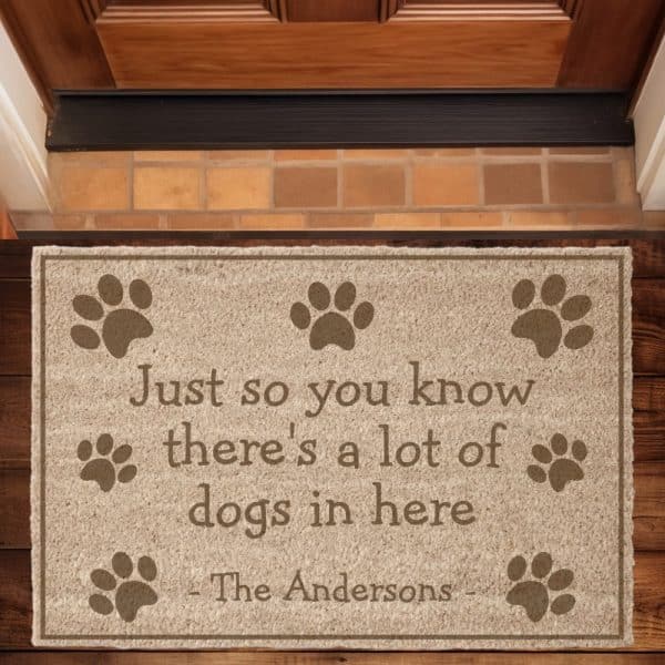 Tan Doormat With The Text Just So You Know There'S A Lot Of Dogs In Here, Signed The Andersons, And Surrounded By Paw Prints.
