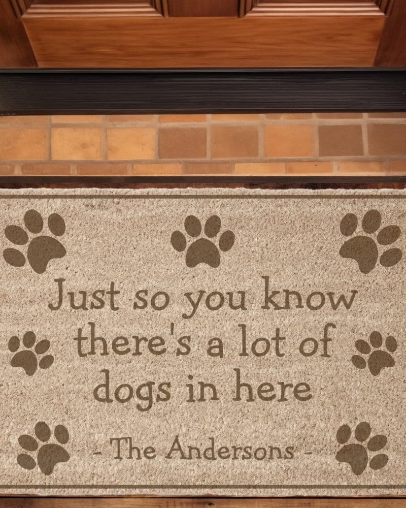 Tan doormat with the text Just so you know there's a lot of dogs in here, signed The Andersons, and surrounded by paw prints.