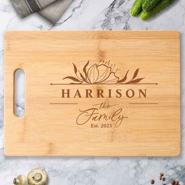 Light Brown Bamboo Cutting Board With A Floral Design And The Engraved Text Harrison The Family Est. 2023.