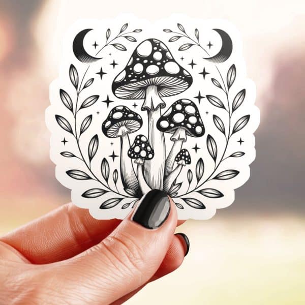 A Hand Holds A Sticker Featuring A Black And White Illustration Of Mushrooms Clustered Together Within A Leafy Wreath, Accented By Stars And Crescent Moons.