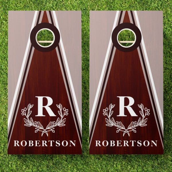 Pair Of Personalized Brown Wooden Cornhole Boards. Each Board Features A Gray And White Triangle Design, A Monogrammed R Within A Wreath, And The Name Robertson.