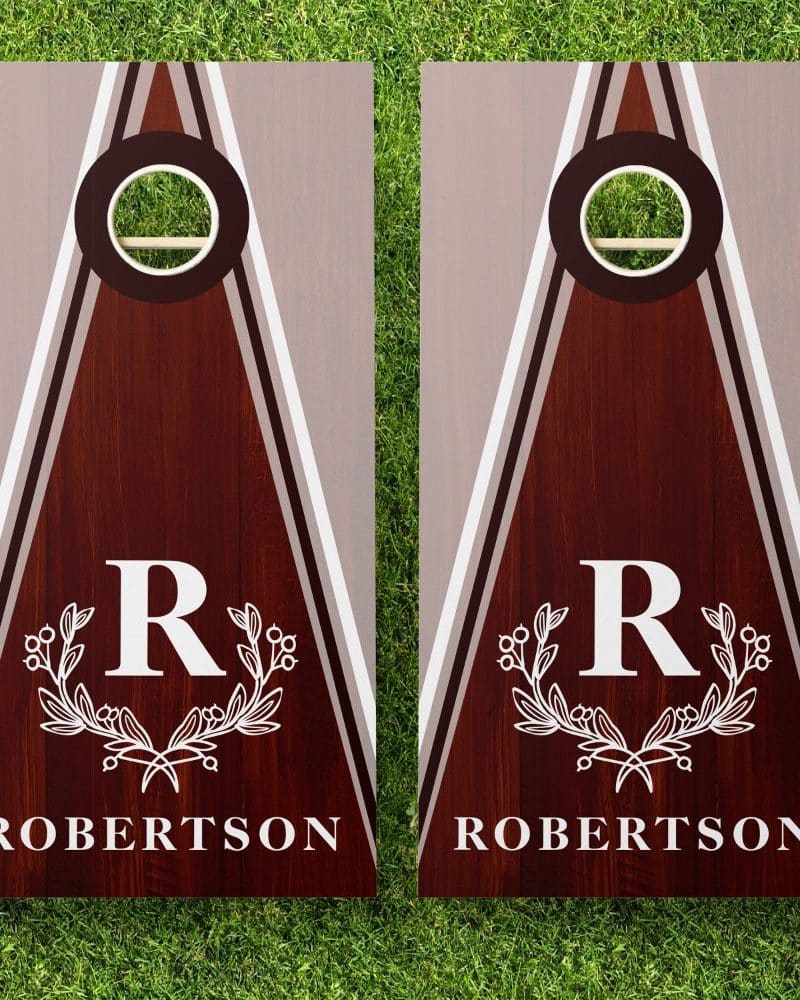 Pair of personalized brown wooden cornhole boards. Each board features a gray and white triangle design, a monogrammed R within a wreath, and the name Robertson.
