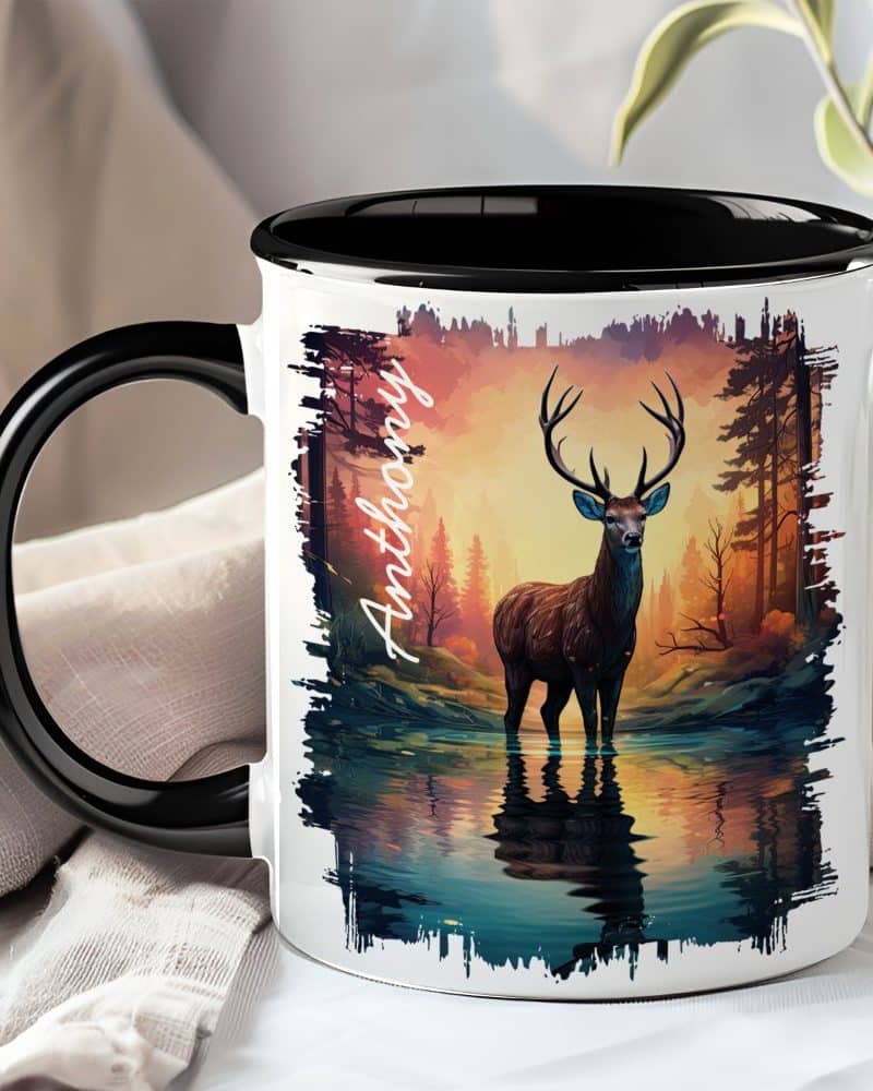 A black-handled mug with a personalized name, Anthony, and a graphic of a deer standing in a tranquil forest reflecting in the water at sunset.