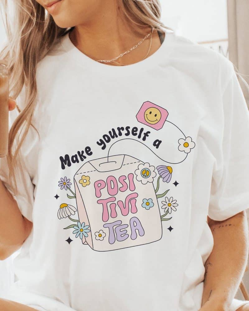 Woman wearing a white t-shirt with a graphic design of a tea bag that says PositiviTea.