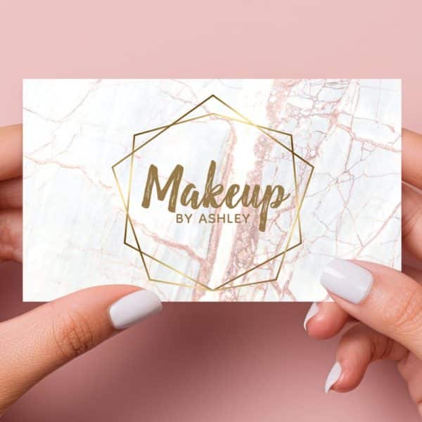 Two Hands Hold A Makeup Artist'S Business Card. The Card Features A Marble Background With A Gold Geometric Frame And The Text Makeup By Ashley.