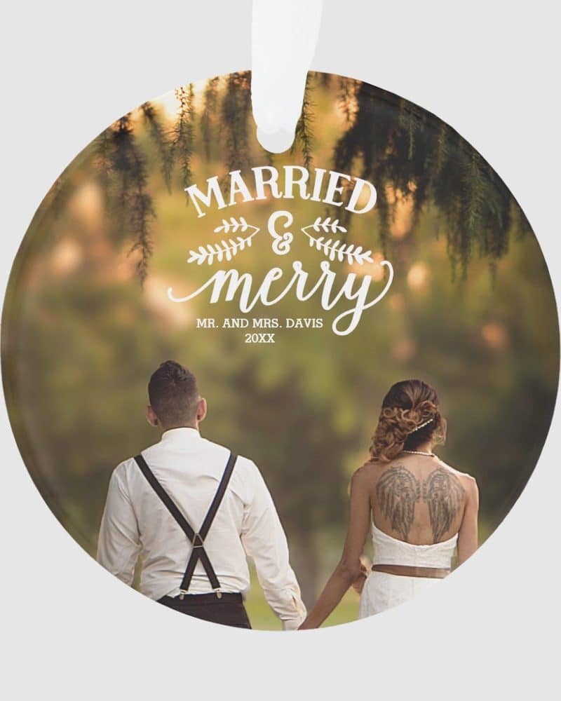 Round wedding ornament featuring a photo of a bride and groom holding hands and walking away from the camera. Text overlay reads Married & Merry.