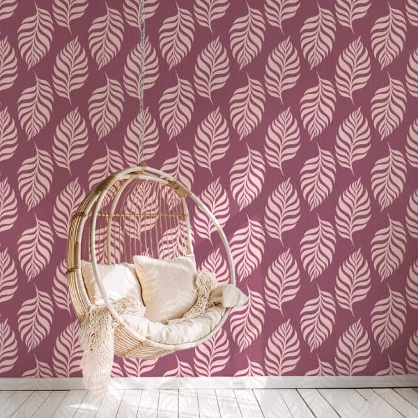 A Hanging Wicker Chair With Cushions Sits In Front Of A Wall With A Pink Leaf Patterned Wallpaper.