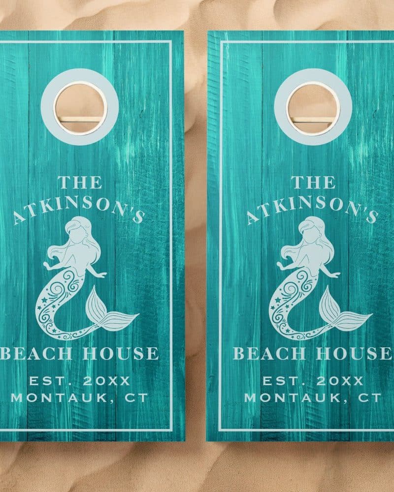Pair of teal cornhole boards with a mermaid design, personalized with the Atkinson's Beach House name and location.
