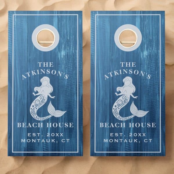 Two Blue Wooden Cornhole Boards, Each Featuring A Mermaid Design, The Family Name Atkinsons, Beach House, And Establishment Year.