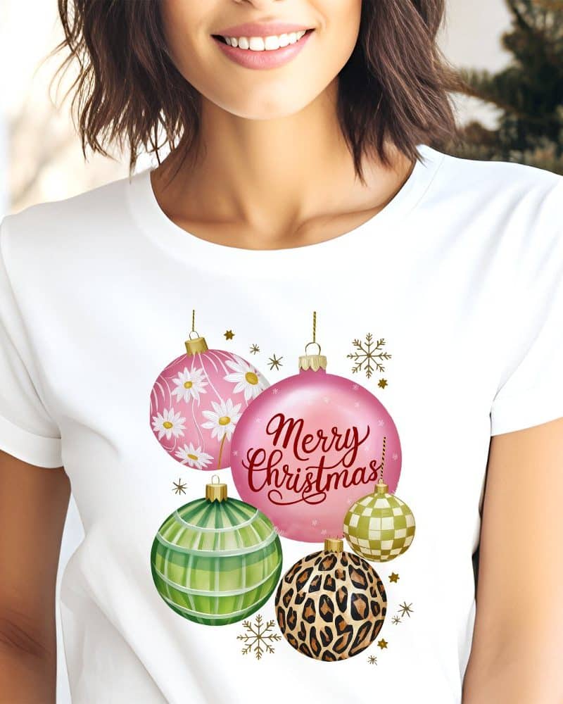 White t-shirt with a Christmas design featuring pink, green, and leopard print ornaments. The words Merry Christmas are printed on the design.