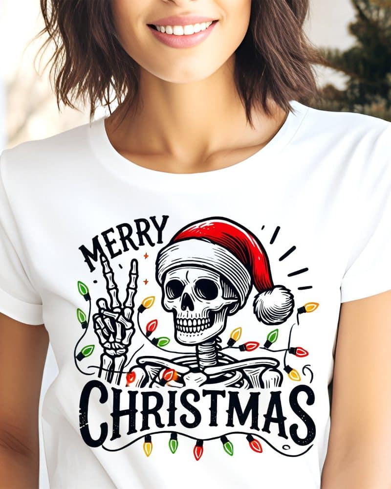 Woman wearing a white t-shirt with a skeleton wearing a Santa hat and giving a peace sign surrounded by Christmas lights. The shirt also says Merry Christmas.