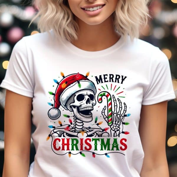 White T-Shirt Featuring A Skeleton Wearing A Santa Hat And Holding A Candy Cane, Surrounded By Christmas Lights. The Text Merry Christmas Is Also On The Shirt.