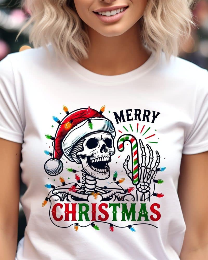 White t-shirt featuring a skeleton wearing a Santa hat and holding a candy cane, surrounded by Christmas lights. The text Merry Christmas is also on the shirt.