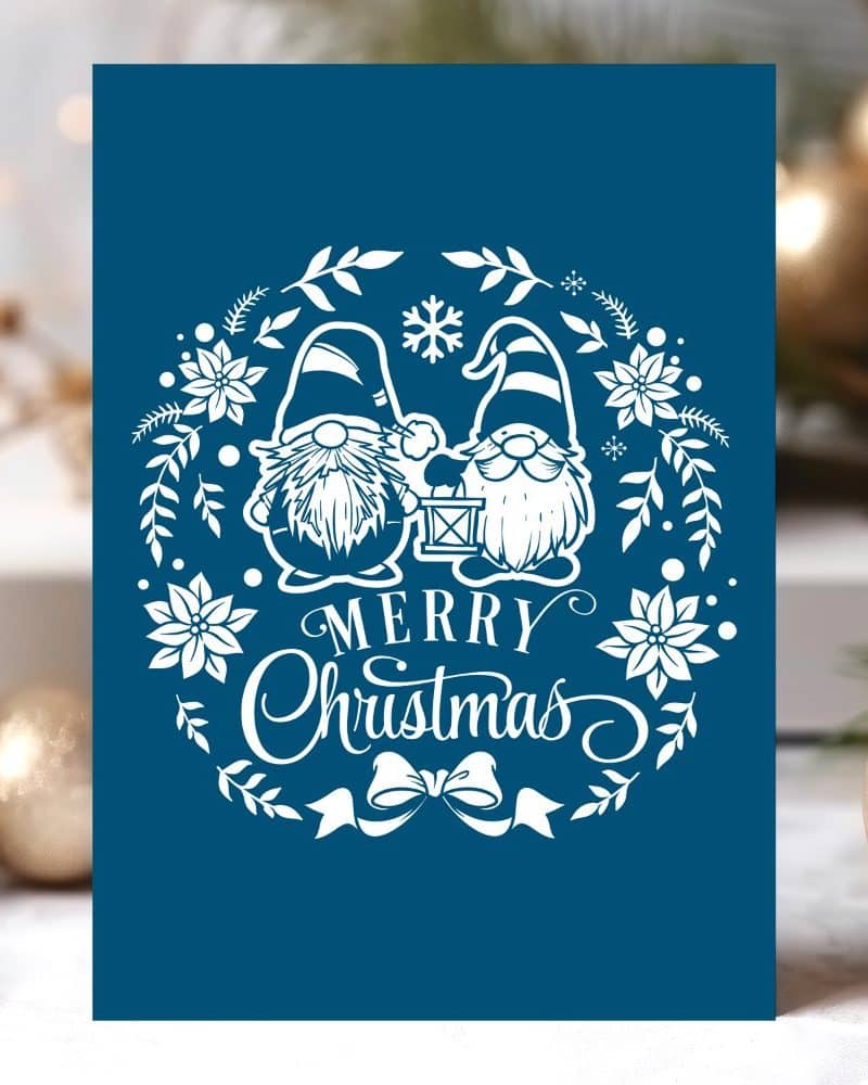 Dark blue Christmas card featuring two gnomes holding a lantern in a white floral wreath with Merry Christmas text.