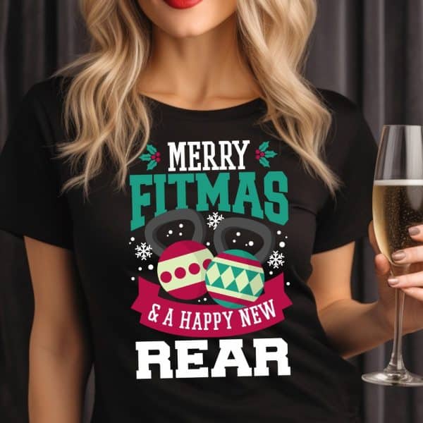 Woman Wearing A Black T-Shirt With A Christmas Fitness Design. The Shirt Says Merry Fitmas And A Happy New Rear. Kettlebells Decorated As Ornaments Are Featured On The Shirt.