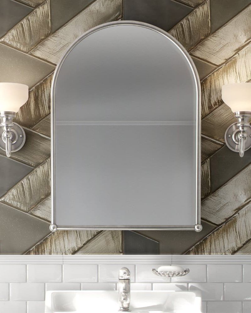 Arch-shaped bathroom mirror with flanking lights, mounted on a herringbone patterned wall.