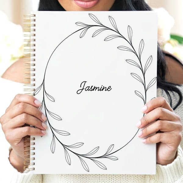 Person Holding A White Spiral Notebook With A Floral Design And The Name Jasmine.